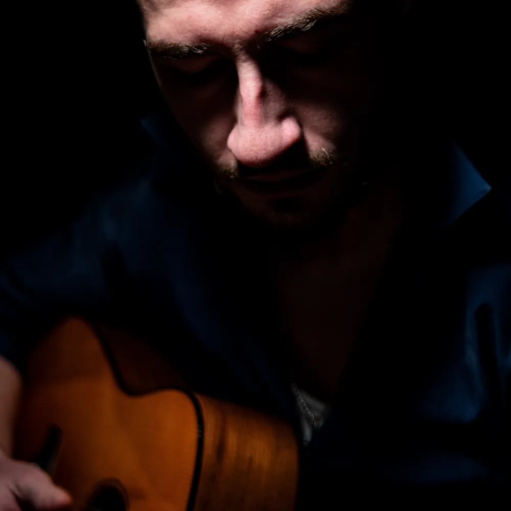 zoomed in photo of a man holding a wooden guitar.